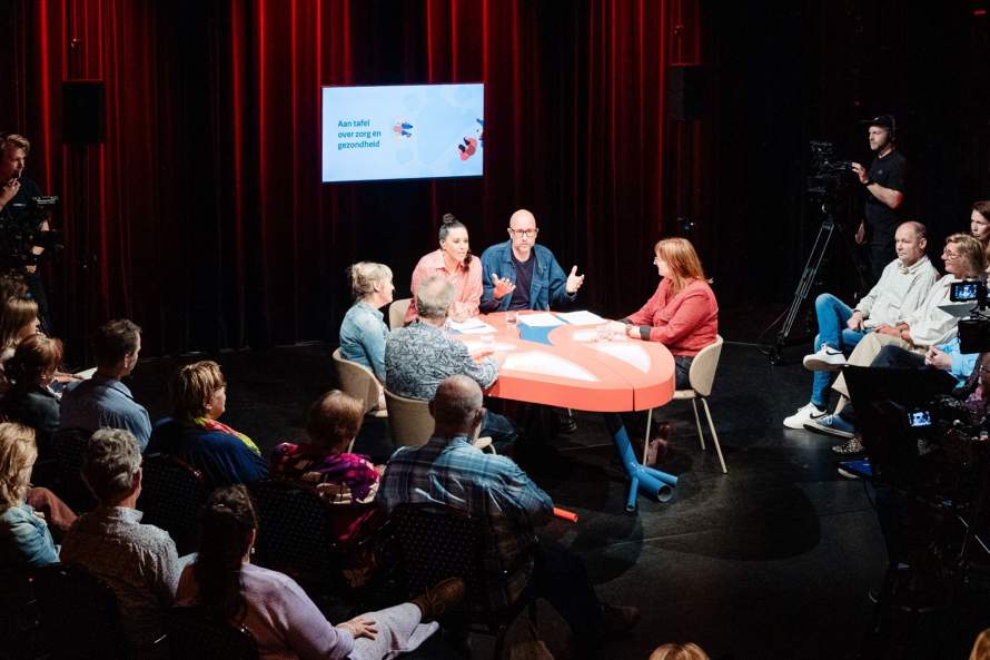 Gespreksparters aan tafel met publiek eromheen