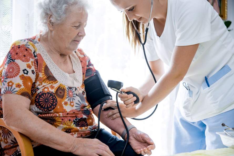 Verpleegkundige meet de bloeddruk bij een oude mevrouw