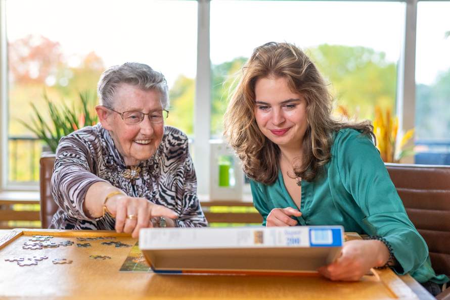 Oude mevrouw en jonge vrouw maken samen een legpuzzel